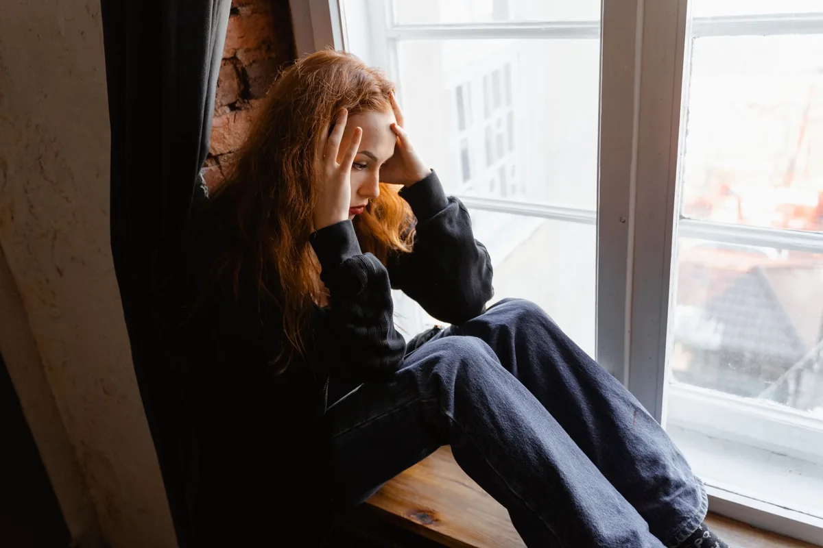 A stressed, anxious woman sitting by a window.