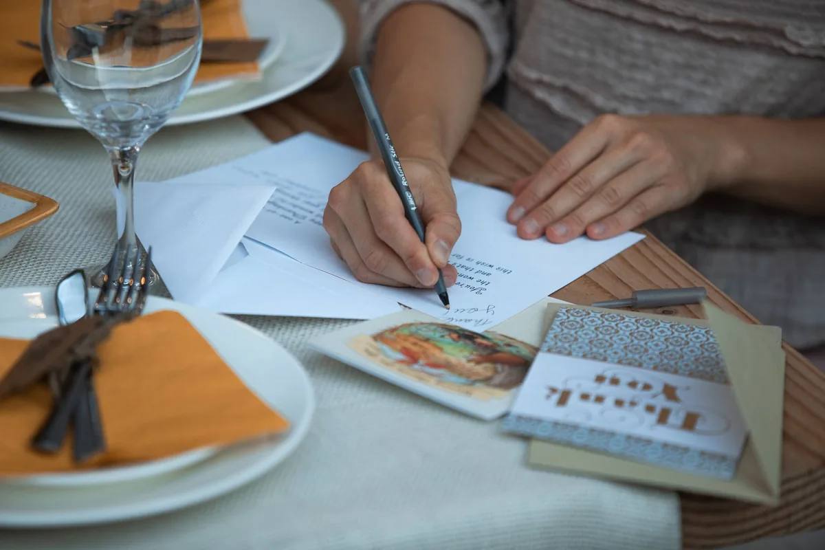 A person writing thank-you notes at a holiday table.