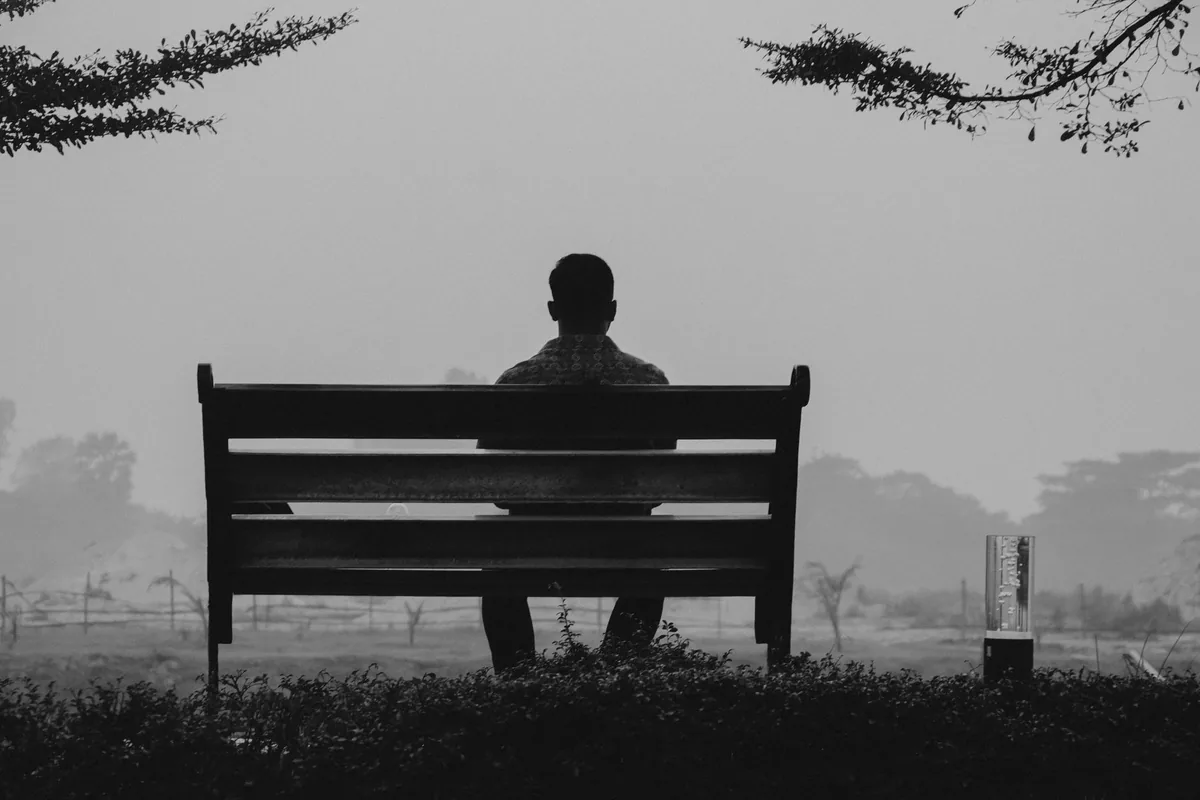 A solitary man sitting alone on a bench in fog.