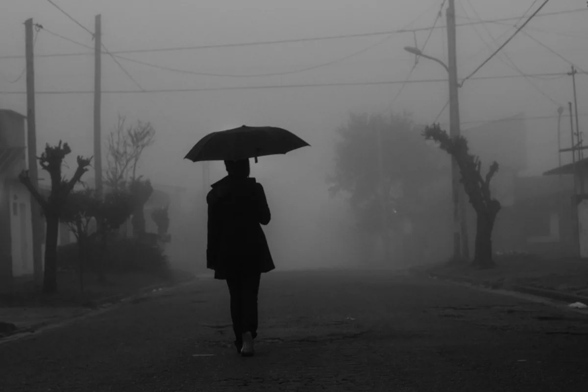 A solitary figure with an umbrella on a foggy street.