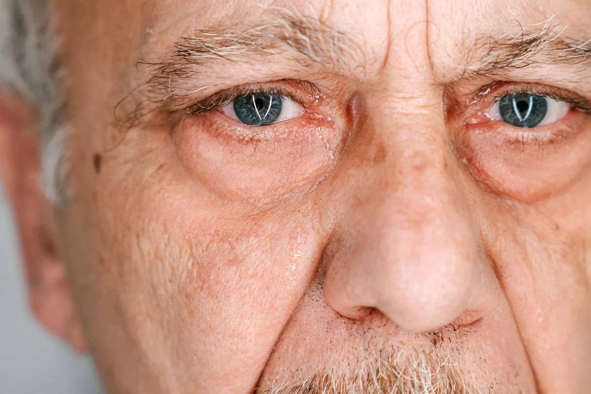 An elderly man with tears on his face, looking sorrowful.